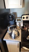 Coffee maker, toaster and kettle on kitchen counter near stove.