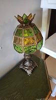 Full side angle of the Tiffany style lamp showing stained glass shade and metal base on green surface.