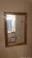 Front view of rectangular gold framed mirror showing full reflection and detailed ornate leaf pattern frame.