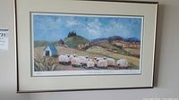 Framed artwork showing a landscape with sheep, a blue-roofed structure, hills and sky