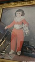 Close-up of framed print showing girl in red clothing with bird on string and cats at feet.