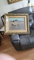 Photo of framed print sitting on a dark gray recliner chair showing full frame and print image of two boys in a field.