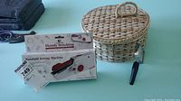 Wicker sewing basket, handheld stitching machine (in packaging), and magnifying glass displayed on a table.