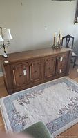 Full view of the large wood sideboard showing the entire piece with decorative top edges and base, placed on a floral rug.
