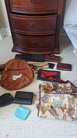 Overview of all wallets, purses, and bags arranged on carpet including a brown handbag and floral butterfly print shoulder bag.