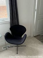 Photo showing one dark grey upholstered, modern swivel chair with a curved back and metal swivel base with four legs, placed near a window and curtain.
