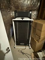 Photo of a black treadmill with white frame and handrails, positioned in a storage space next to cardboard boxes.