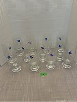 12 clear Studio Nova beer glasses arranged in a group with blue logo stickers visible on each glass.