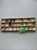 Overview of assorted costume jewelry pieces organized in a wooden tray with multiple compartments showing earrings, charms, and necklaces.