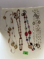 Photo showing five long necklaces laid flat, with varying bead shapes and colors on a white surface.