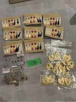Photo showing several sets of earrings on fashion earring cards with diamond shapes in white, red heart studs, yellow teardrop studs, and black geometric drop earrings, several metal hoop earrings, and gold round disc earrings in plastic bags.