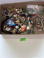 Full view of box filled with assorted costume jewelry pieces including bracelets, earrings, necklaces, brooches, beads, and pins.
