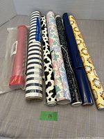 Side view of all craft rolls laid out, showing color and pattern variety including red faux leather, blue and white stripes, cow print, flowers, speckled black, navy blue, and Garfield print.