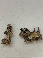 Front view of two dog brooches on white background showing poodle and Scottish terrier designs