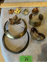 Top view showing all pieces: leaf-shaped brooches, cuff bracelets, bangles, heart brooch, with ruler for scale.