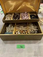 Jewelry box with top and bottom compartments filled with various bead necklaces and bracelets, inside yellow satin-like fabric lining on lid