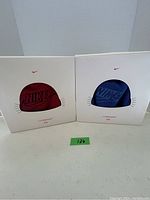 Two white retail boxes side-by-side, showcasing red and blue Nike toques with headphone technology for kids, packaged and new looking.