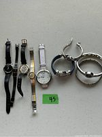 Eight ladies watches with several styles of bands and faces alongside one silver cuff bracelet on a flat surface.