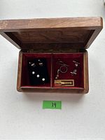 Top view of open wooden jewelry box showing compartments and contents including cuff links, tie pin, and studs.