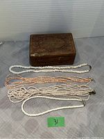 Four beaded necklaces and carved wooden jewelry box arranged on a fabric surface.