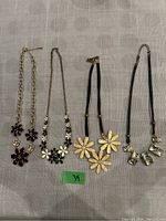 Four necklaces laid out on fabric showing different styles and colors of flower and glass pendant necklaces.