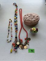 Photo showing three distinct necklaces laid out next to a pink embossed oval jewelry box and a small porcelain floral trinket box.