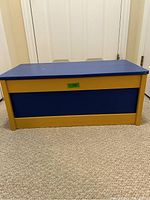 Front view of the painted wooden toy box showing blue and yellow/gold paint.