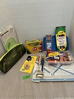 Wide view of all school supplies including crayons, pencil case, writing instruments, erasers, sharpener, and paper pads