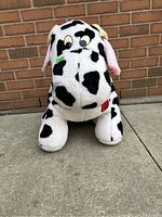Front view of the large stuffed cow showing its face with black spots and colored patches.