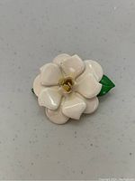 Front view of the tin flower brooch showing white enamel petals with a yellow center and two green enamel leaves.
