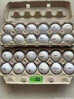 Photo showing 24 used golf balls displayed in 2 cardboard egg cartons, mixed brands and numbers visible.