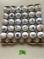Top-down photo of 30 white logo golf balls arranged in an egg carton holder showing various corporate logos.