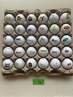 Thirty used golf balls each with a different logo, arranged in rows in a cardboard tray, showing a variety of corporate logos including Kellogg's, Amoco, Wilson, Arla, and others.
