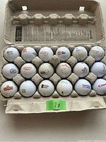 Photo of 18 used golf balls in a recycled cardboard holder showing different company logos on each ball.
