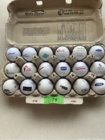 Photo of 18 used golf balls with various corporate logos displayed inside a large egg carton