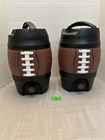 Front view of two football-themed water jugs showing details and spigots