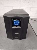 Front view showing the LCD display panel lit with attention warning, APC logo, and model Smart-UPS C1500 label.