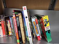 Books arranged on a shelf with visible titles such as 'The Greatest Moments in Sports', 'The Elements', 'The Night Before Christmas', 'The Visual Dictionary', and a Marvel Character Encyclopedia.