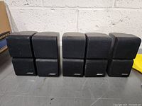Front view of all 5 Bose speakers showing black fabric grills with Bose logo, arranged in a row.