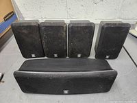 Front view of five Boston speakers including four satellite and one center channel speaker all with black fabric grilles and Boston logo.