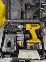 Yellow DeWalt 18V XR cordless drill with battery installed, charger with cord, and instruction manual inside black carrying case.