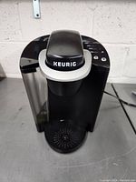 Front view of black Keurig single-serve coffee maker with water reservoir and Keurig logo visible.