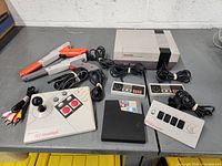 Nintendo NES console with accessories and controllers on a grey surface with a white wall background.