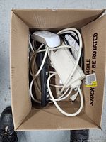 Top-down photo of box containing assorted power strips and outlet extension cords tangled inside.