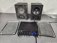 Photo of the Pyle stereo amplifier with two black speakers and their removed grills on a flat surface.