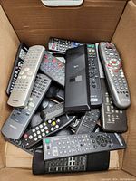 Box of multiple remote controls from different brands including Toshiba, Sony, Xfinity, RCA, and others.
