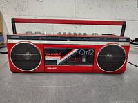 Sharp QT12 portable radio cassette player showing front with speakers, cassette door, and handle.