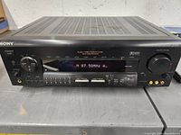 Front view of Sony STR-DE915 Audio/Video Control Center powered on showing radio frequency on display and control buttons.