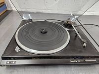 Front view of Technics turntable with clear dust cover open showing platter and tonearm.