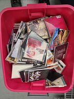 Top-down view inside pink tote showing many music CDs in standard jewel cases, some cover art visible including portraits and graphic designs.